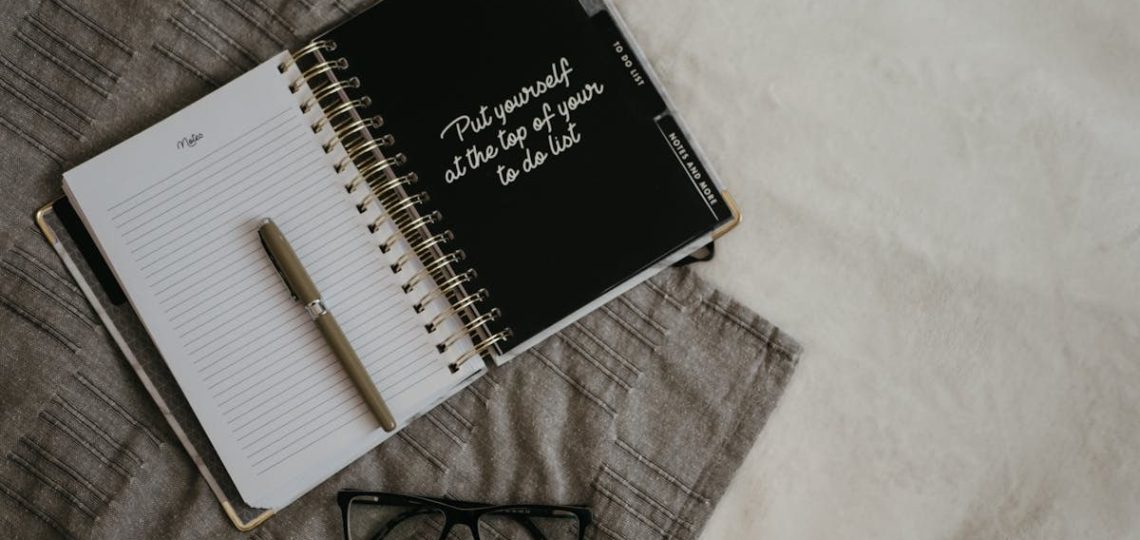 Stylish flatlay featuring a planner with quote, pen, and eyeglasses on a neutral background.